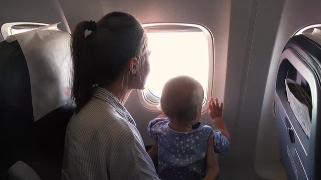 Mom and her baby in airplane look out the window