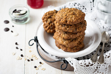 Stack of oatmeal cookies with chocolate on a light background with flakes and a bottle of milk. Selective focus.