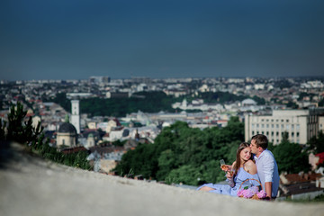 Fototapeta na wymiar Man and woman drink champagne sitting on the plaid with great cityscape behind them