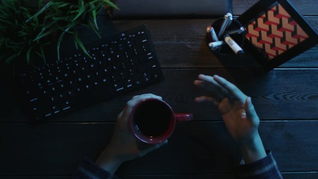 Overhead view of man gesticulating in front of computer with cup of tea in his hand