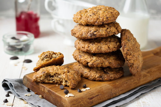 Stack of oatmeal cookies with chocolate on a light background with flakes and a bottle of milk. Selective focus.