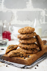 Stack of oatmeal cookies with chocolate on a light background with flakes and a bottle of milk. Selective focus.