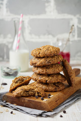 Stack of oatmeal cookies with chocolate on a light background with flakes and a bottle of milk. Selective focus.