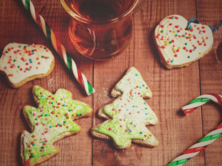 Cup mug of tea, gingerbread in the form of a Christmas tree and candy canes on a wooden background. Toned photo.