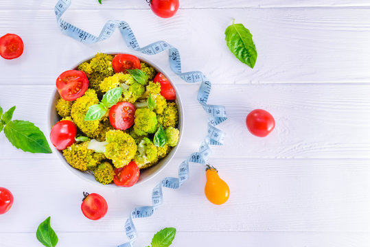 Top view Salad Bowl with cherry tomatoes, broccoli, fresh ingredients, measuring tape on the white wooden background. Healthy lifestyle concept. Detox, diet, vegitarian. Selective focus. Text space.
