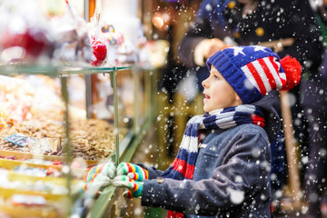 Little kid boy with gingerbread and sweets stand on Christmas market