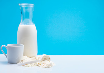 Bottle of fresh milk with powdered milk and spoon for baby on white table,blue background.
