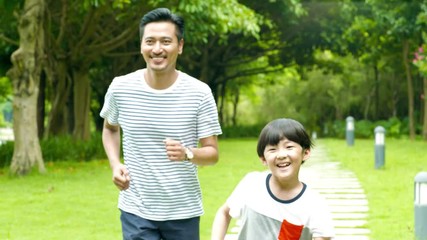 asian father running behind his son in park in summer in slow motion - Powered by Adobe