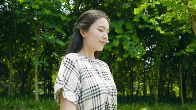 pretty asian woman taking deep breath, smiling & enjoying nature outdoor