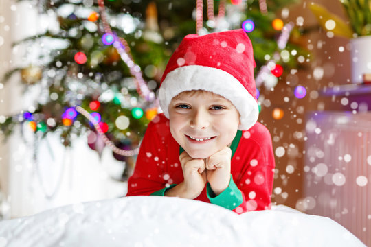 Little kid boy in santa hat with Christmas tree and lights on background.