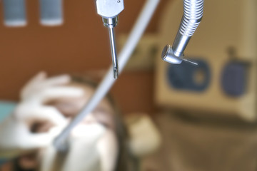 Dental drill on the foreground with teen girl patient being treated on the blurred background 