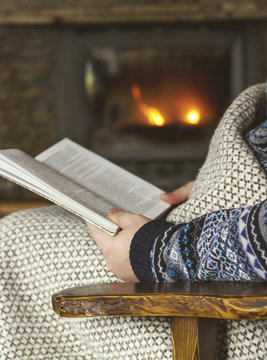 Man reading a book, sitting in a rocking chair with knit plaid in front of a fireplace