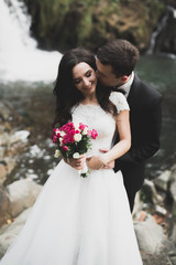 Beautifull wedding couple kissing and embracing near the shore of a mountain river with stones