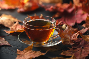 Cup of tea with autumn leaves background on wooden table / fall tea background