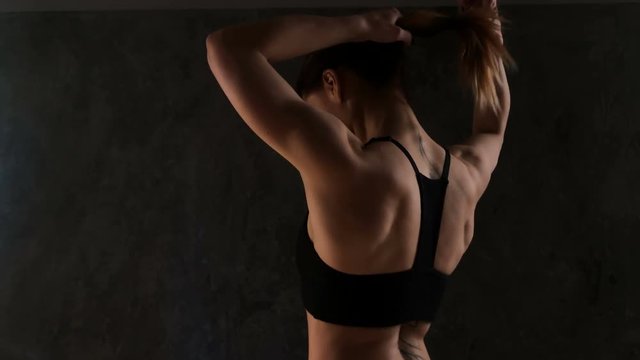 Sexy and fit woman preparing for training over dark background. Woman put her hair in a bundle before exercises in a gym