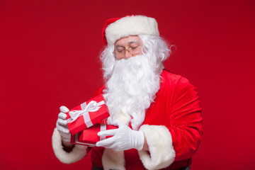 Christmas. Photo Santa Claus giving xmas present and looking at camera, on a red background