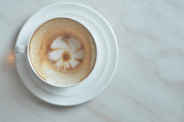 Cup cappuccino is Finished drink(with a flower pattern on the surface) on White marble table.