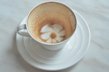 Cup cappuccino is Finished drink(with a flower pattern on the surface) on White marble table.