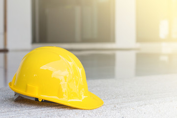 The yellow safety helmet put on the blueprint at construction site with crane background