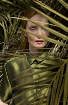 young woman in green clothes behind palm leaves