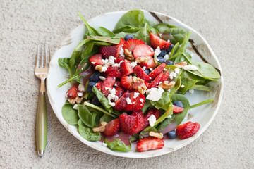 Strawberry blueberry walnut spinach salad topped with a raspberry olive oil vinaigrette dressing and crumbled feta cheese top view
