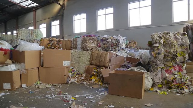 Pile of waste carton for recycling, closeup view in motion. Big Factory For Recycling Paper and Carboard. Large bales of waste paper are compressed and ready for processing.