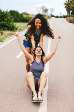 Young multiethnic female friends having fun skating on the street in summer.