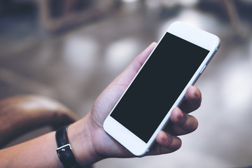 Mockup image of a woman's hand holding white mobile phone with blank black screen , concrete floor background