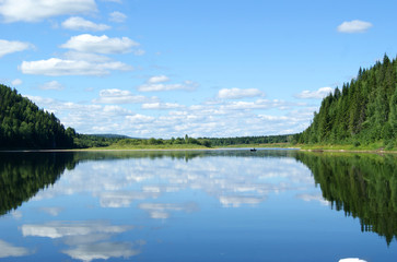 landscape: the Ural river Vishera in clear weather, the calm water reflects the wooded shore and the sky with clouds..