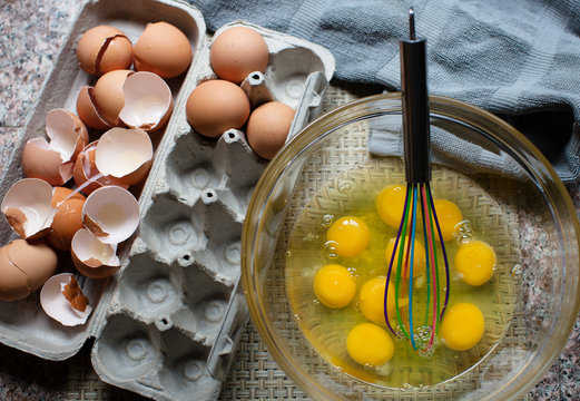 Many raw eggs in a bowl with the shells off to the side