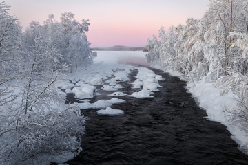 Winter river, surrounded by trees, in Finland at sunset