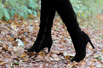 Women's legs in boots on leaves. Beautiful long female legs in black boots against a background of yellow autumn leaves. women's shoes on the autumn street