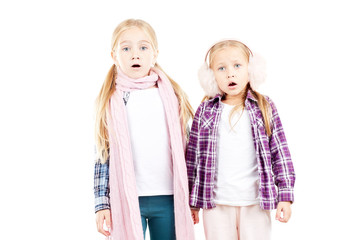 Portrait of two little sisters wearing scarf and earmuffs posing against white background