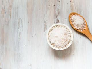 Plakat white bowl with large sea salt and wooden spoon on white wooden table. Top view with copy space for text.