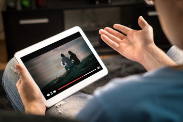 Loading icon rolling on video in an online movie streaming service. Bad and slow internet connection. Film player stopped. Frustrated and confused man watching and holding tablet while spreading arms. - obrazy, fototapety, plakaty