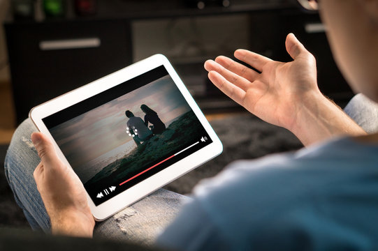 Loading icon rolling on video in an online movie streaming service. Bad and slow internet connection. Film player stopped. Frustrated and confused man watching and holding tablet while spreading arms.