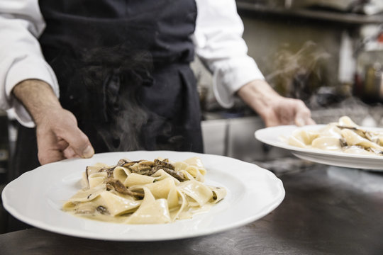 Chef holding two plates of pappardelle pasta with mushrooms