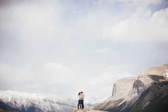 Engaged couple standing and hugging with mountain backdrop at Lake Minnewanka in Banff National Park