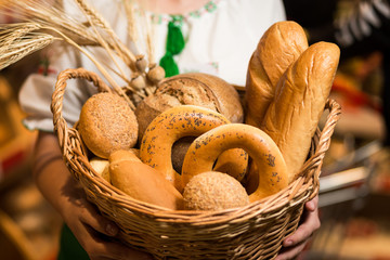 Woman holding bread in basket,Composition with variety of baking products on wooden table. Bread and buns inside basket. Fresh bakery products on table.Cereal products. Bakery and grocery concept