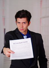 Close up of boss wearing a suit and giving a sheet of paper of termination of contract text on it, in a blurred background