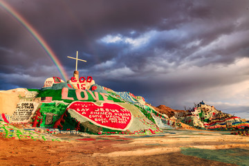 A storm and a rainbow descend upon California's famous Salvation Mountain outside of Slab City.