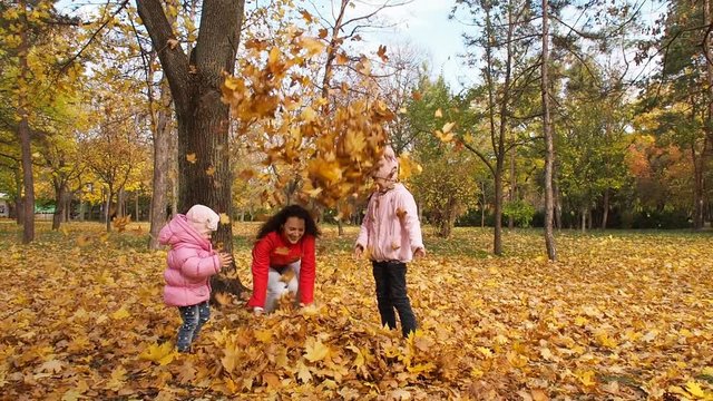 Happy family in autumn park. Mother with children playing with yellow leaves.