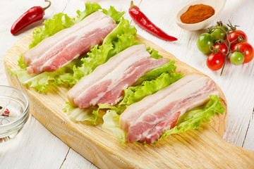 Raw pork meat brisket bacon on chopping board with lettuce and spices