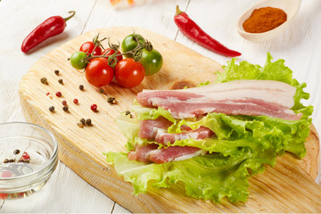 Raw pork meat brisket bacon on chopping board with lettuce cherry tomatoes spices