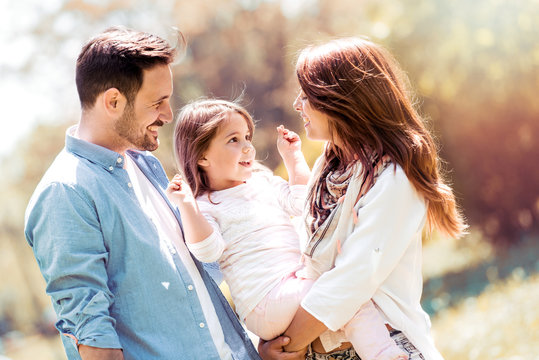 Happy Family In Park On Sunny Day. Mother, Father And Daughter.