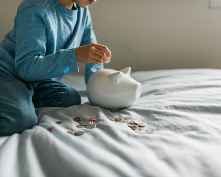 Boy inserts a coin into his piggy bank while sitting on the bed