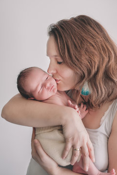 Mother holding her newborn baby in her arms and gently kissing his cheek.