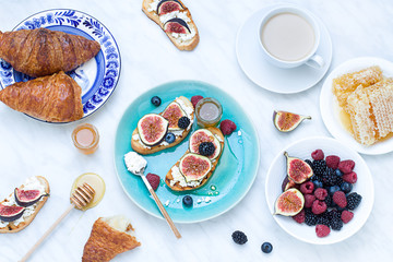 Morning breakfast with italian bruschettas with fresh ripe summer berries, figs, cheese, honey, honeycomb, french croissants and a cup of cofffe. Flat lay. top view