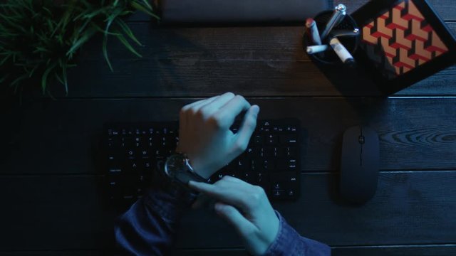 Overhead shot of man putting off his watch and typing on keyboard