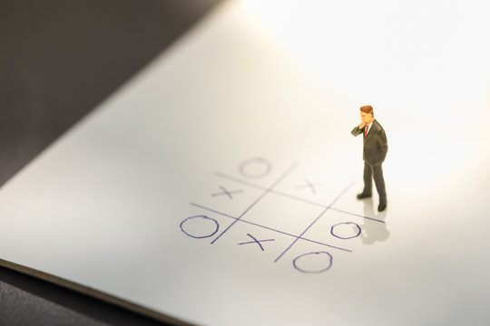 Business direction and planning concept. Businessman miniature figure standing and thinking on paper with OX (tic tac toe) board game.